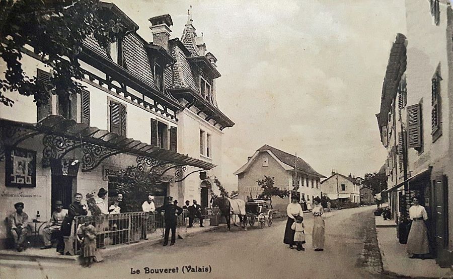 Terminus : Collection Jean-Charles Bussien - Scène du village devant le restaurant Le Terminus au début des années 1900 : l'atmosphère d'une époque révolue résonne à travers cette ambiance et les façades historiques