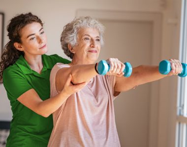Senior woman using dumbbells with physiotherapist